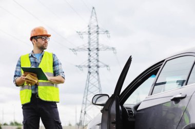 Kasklı ve üniformalı bir adam, sahada bir elektrikçi. Profesyonel elektrik mühendisi elektrik hatlarını inceliyor..
