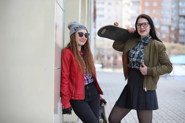 一个年轻的时髦女孩正在骑滑板 女孩的女朋友散步在城市与滑板 在街上的春季运动与滑板 — 图库照片