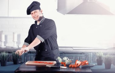 Adam mutfak masasında sebze pişiriyor.