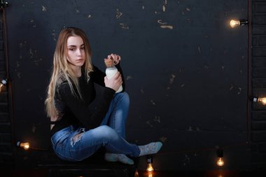 Genç kız, siyah bir duvardaki şişeden süt içiyor.