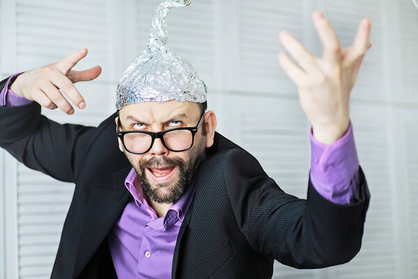 Bearded funny man in cap of aluminum foil. Concept art phobias. Conspiracy theory. Conspiracy. Insanity.