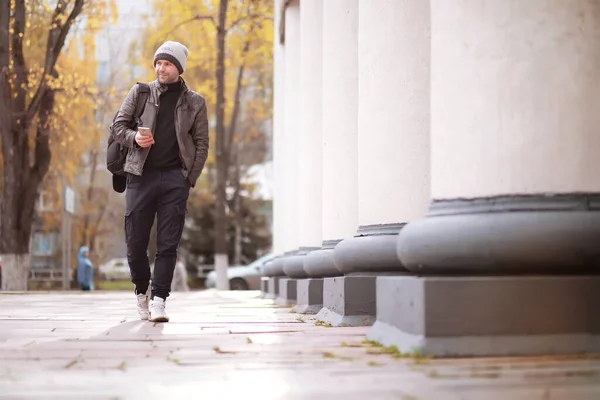 Autumn concept. A man walks through the city. Autumn leaves on footpath