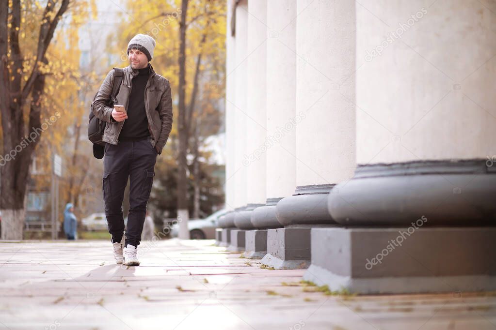 Autumn concept. A man walks through the city. Autumn leaves on footpath