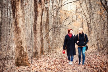 Annesiyle sonbahar bahçesinde yürüyen genç bir kız.
