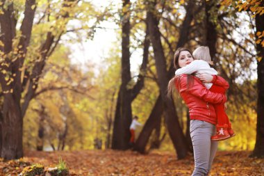 Genç bir aile güneşli bir günde sonbahar parkında yürüyüş yapıyor. Birlikte olmanın mutluluğu..