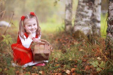 Kırmızı şapkalı ve elbiseli küçük bir kız parkta yürüyor. Masal kahramanı için kostüm Kırmızı Başlıklı Kız