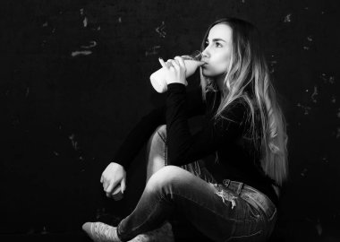 Genç kız siyah duvardaki bir şişeden süt içiyor.