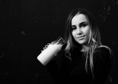 Genç kız siyah duvardaki bir şişeden süt içiyor.