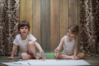 Küçük çocuklar tuvalette büyük bir kağıt parçasına resim yaparlar.