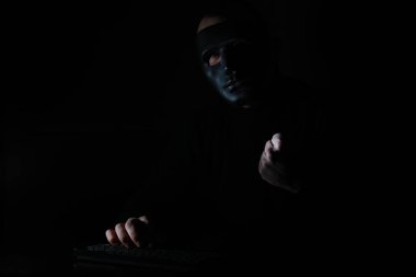 Dar bir masada maske takan bir adam klavyeye baskı yapıyor.