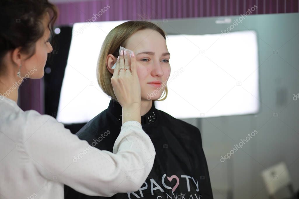 Young girl with a make-up artist in the studio in front of a mirro