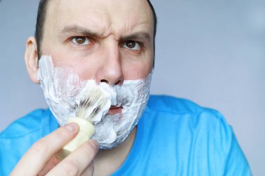 Bir adam aynanın önünde tıraş olur. Tıraş köpüğü. Tek kullanımlık jilet..