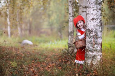 Kırmızı şapkalı ve elbiseli küçük bir kız parkta yürüyor. Masal kahramanı için kostüm Kırmızı Başlıklı Kız