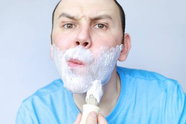 Bir adam aynanın önünde tıraş olur. Tıraş köpüğü. Tek kullanımlık jilet..