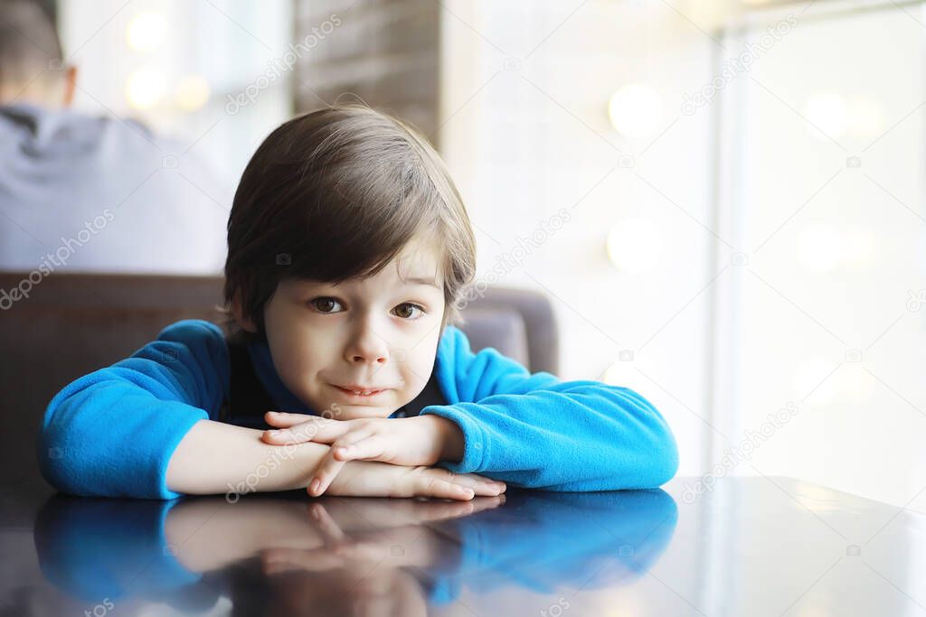 A young boy sits at a table near the window in cafe and waits for a waiter to come up and take an order.
