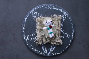 Taştan bir arka planda dramatik ışıklandırmayla vudu bebeği. Büyülü bebeklerle, tarot kartlarıyla, kitaplarla, şeytani mumlarla ve cadılık objeleriyle dolu mistik bir hayat. Kehanet ayini.