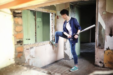 Terk edilmiş bir binada elinde beysbol sopası olan genç bir adam.