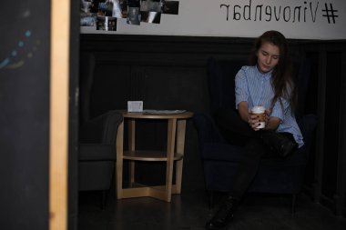 Kahve kızla. Genç güzel kız bir kafede oturan ve kağıt bardak kahve içme. Kız kahvaltı kahve evinde geçiriyor