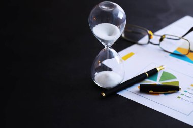 Kum saati ampulleri arasında koşan ve bir geri sayım bitiş tarihine kadar geçen zamanı ölçen, fotokopi alanı olan karanlık bir zemin arka planında..