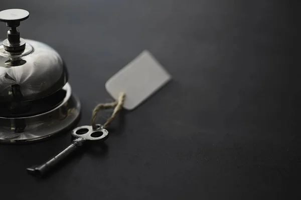 A shiny silver metal bell at hotel reception. A table in the hotel at the concierge with a bell and a door key. Key and bell in a hotel.