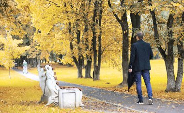 Gözlüklü genç bir adam yağmur sırasında elinde şemsiyeyle parkta yürür..