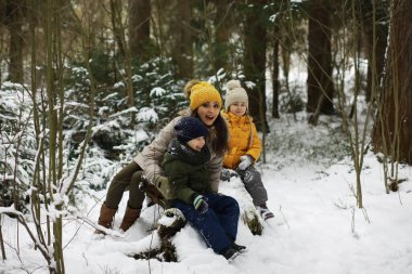 Mutlu bir aile kışın dışarıda karda oynar ve güler. Şehir parkı kış günü.