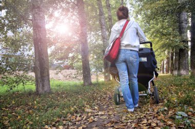 Anne bebek arabası ile sonbahar park sokakta yürüyor