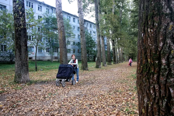 用婴儿车的妈妈走在秋天的公园小巷 — 图库照片