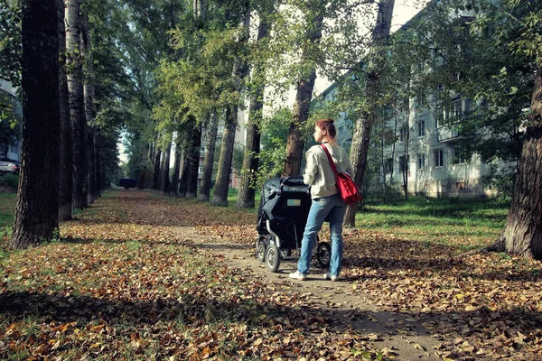 Мама з коляскою гуляє по провулку осіннього парку — стокове фото