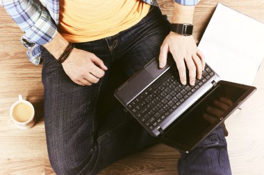 Yerde dizüstü bilgisayarı olan bir adam var.