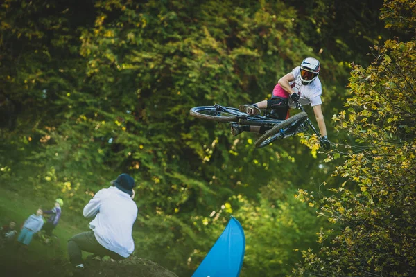 Frontal shot of a mountain biker jumping over a dirt jump in a bike park performing a tail whip .