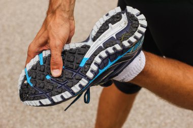 Bir adam koşu ayakkabısının lastiğini kontrol ediyor. Bir bacağının üzerinde duran bir adam ve diğer bacağı koşu ayakkabısındaki ya da spor ayakkabısındaki ipliği ortaya çıkarmak için eğilmiş..