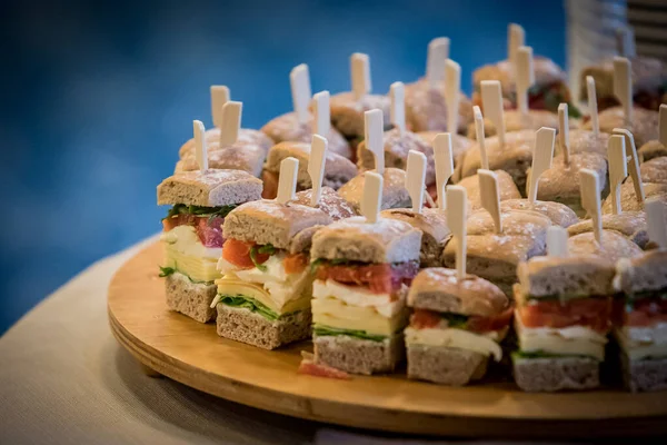 Small sandwiches from a catering service on a conference. Sandwiches with bread, salmon, cheese, pepper and so on, served on a plate.