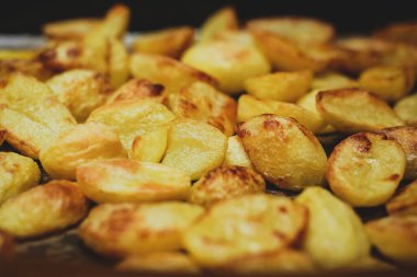 Fırındaki bir tabağın üzerindeki patates parçalarının detaylı görüntüsü. Lezzetli altın, sarı ve kabuklu patates.