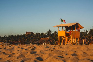 Puerto Escondido, Meksika 'daki tipik sahil manzarası plaj evi, altın kum, ağaçlar ve mavi gökyüzü. Meksikalı cankurtaranlar görev başında.