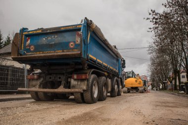 Mavi 4-4 eksenli damperli kamyon bir kasaba yolundaki şantiyede bir sonraki görevini bekliyor. Kamyonun arkası görünüyor..