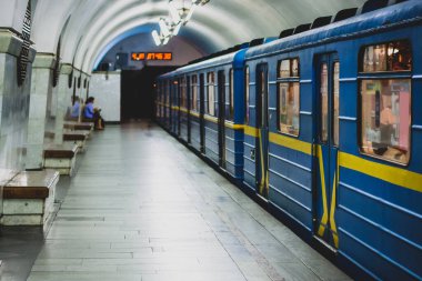Mavi ve sarı renkli metro ya da yeraltı treni Ukrayna 'nın Kiev kentindeki bir metro istasyonundan ayrılıyor. Platformda bir yolcu görülüyor..