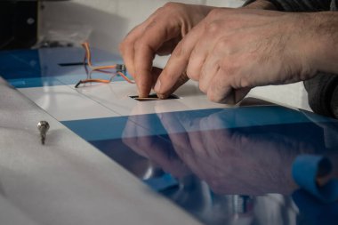 Bir uçak modelinin kanadında servo RC motor monte ederken görülen birinin elleri. Mavi renkte kanat, arka planda bağlantı kabloları görülüyor.