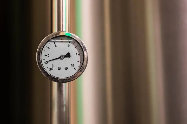 A pressure gauge, manometer, filled with liquid and showing around 1bar of pressure on a stainless background.