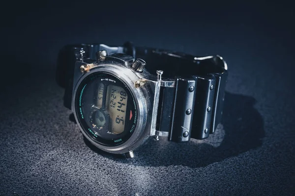 Steampunk looking digital wrist watch lying on the grainy textured table. Shiny metal wrist watch with rubber strap.