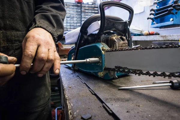 人は機械工の店の作業台でチェーンソーの刃をねじ込んでいる 見たチェーンのサービス サイズとブレードを削除13ツールスパナ — ストック写真