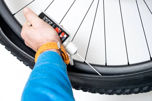 A person is pouring a tubeless milk fluid into a carbon wheel of a mountain bike. Hand squeezing a tubeless milk bottle.