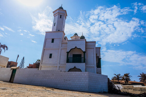 Grand Mosque de Warar, white and green islamic church on the edge of the beach in Tonghor, Dakar, on a sunny day with some clouds.