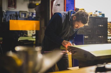 Genç bir erkek, bir ev atölyesinde klasik bir araba kapısında bir açı öğütücü kullanıyor. Bir arabayı farklı araçlarla çalıştırma ve restore etme kavramı.