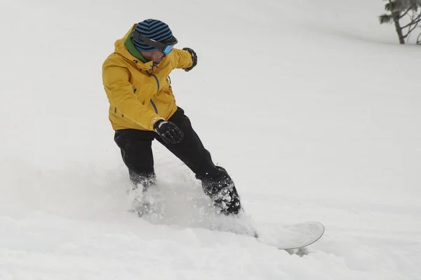 ジャンプの間に下り坂に行く雪の中でスノーボーダー 黒いズボンとオレンジボードに乗って雪の上に曇りの日にジャンプして黄色の服でボーダー — ストック写真