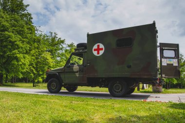 Eski bir askeri kurtarma ambulansı, yeşil alana kırmızı haçla boyanmış, kamuflaj renginde..