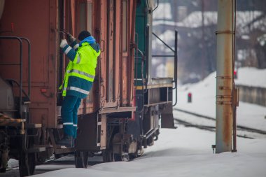 Koruyucu yansıtıcı giysiler içinde demiryolu işçisi karlı bir günde hareket halindeki bir trene tırmanıyor..