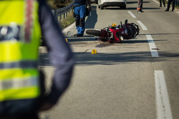 Car and a red sport motorcycle crash scene on an open road in afternoon. Workers and police seen around the crash site, with a queue of traffic building behind. Destroyed van and motorcycle.