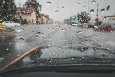 Arabanın ön camına yağan yağmur kavşağı ve kırmızı ışığı engelliyor. Islak ve kirli ön cam yüzünden yolda tehlikeli bir durum var.