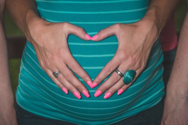 İki kadın bir arada, biri eli hamile karnında kalp şeklinde duruyor. Lezbiyen ya da aynı cinsiyetten insanların çocuk sahibi olması kavramı. Güzel bir sembol, elleri göbeğinde..